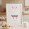 Welkomstbord Aqiqah in witte lijst op een marmeren blad, naast roze en groene macarons en cakepops.