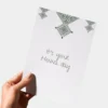 Hand die een witte wenskaart vasthoudt met daarop 'It's your Henna day' geschreven in een sierlijk handschrift.