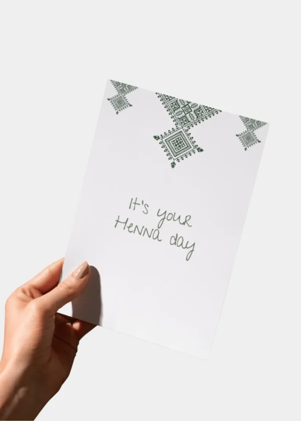 Hand die een witte wenskaart vasthoudt met daarop 'It's your Henna day' geschreven in een sierlijk handschrift.